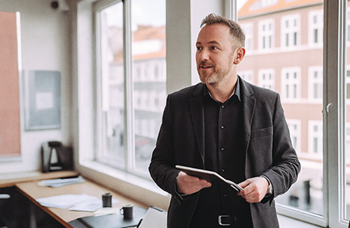 Jens - Driftschef med iPad i skandinavisk kontor og vinduesudsigt_500x325